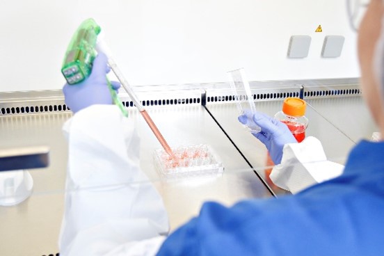 Scientist in blue and white gown and blue gloves using an IPSC Line with samples