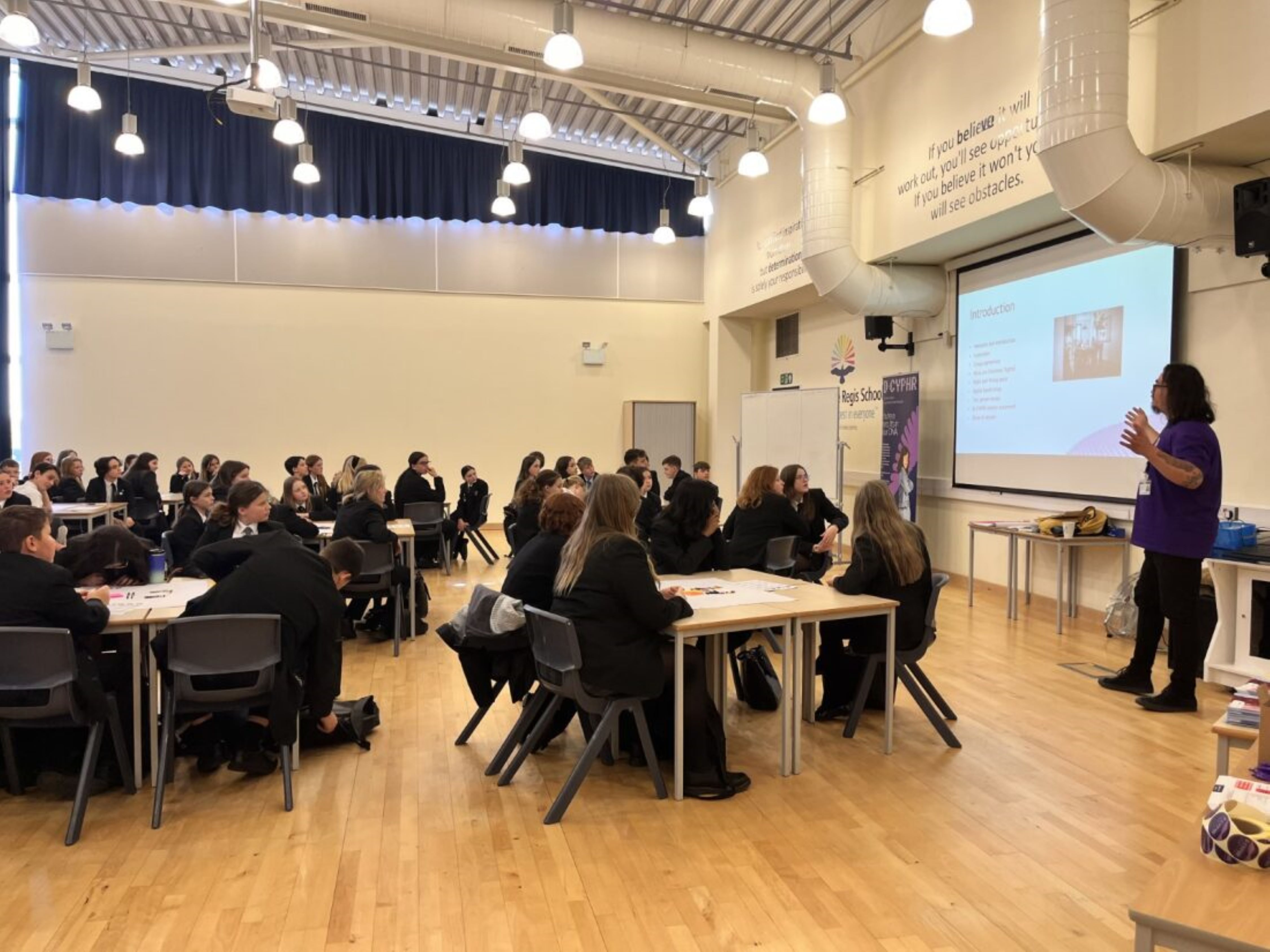 George standing at the front of classroom presenting to large group of school students