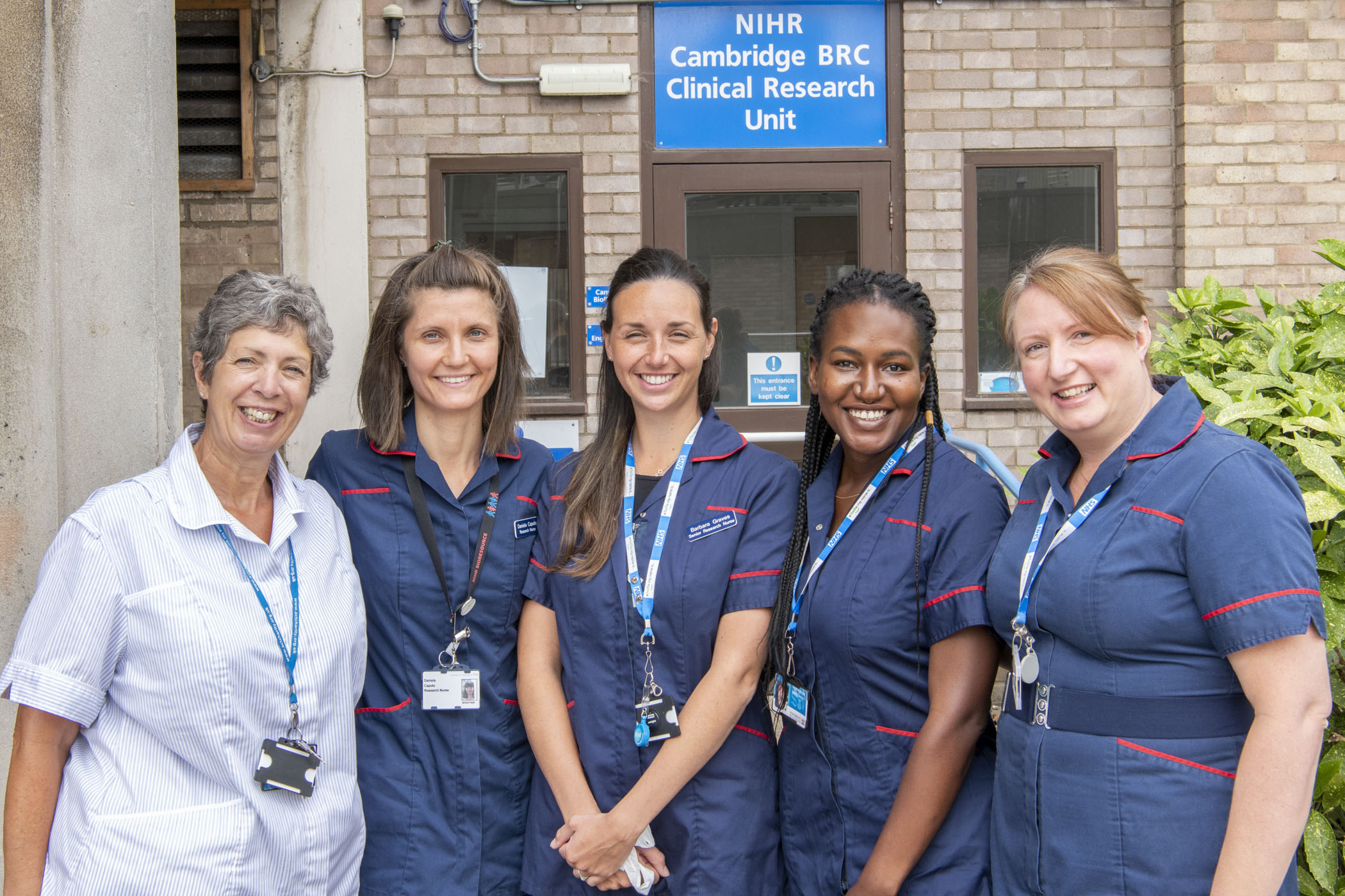 From left to right, Gillian, Dani, Barbara, Aisha and Emma from our clinical team all smiling in nursing uniform outside our Clinical Research Unit building 