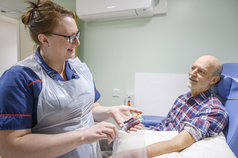 Volunteer seated looking at nurse who is holding vials of blood and putting them into a bag