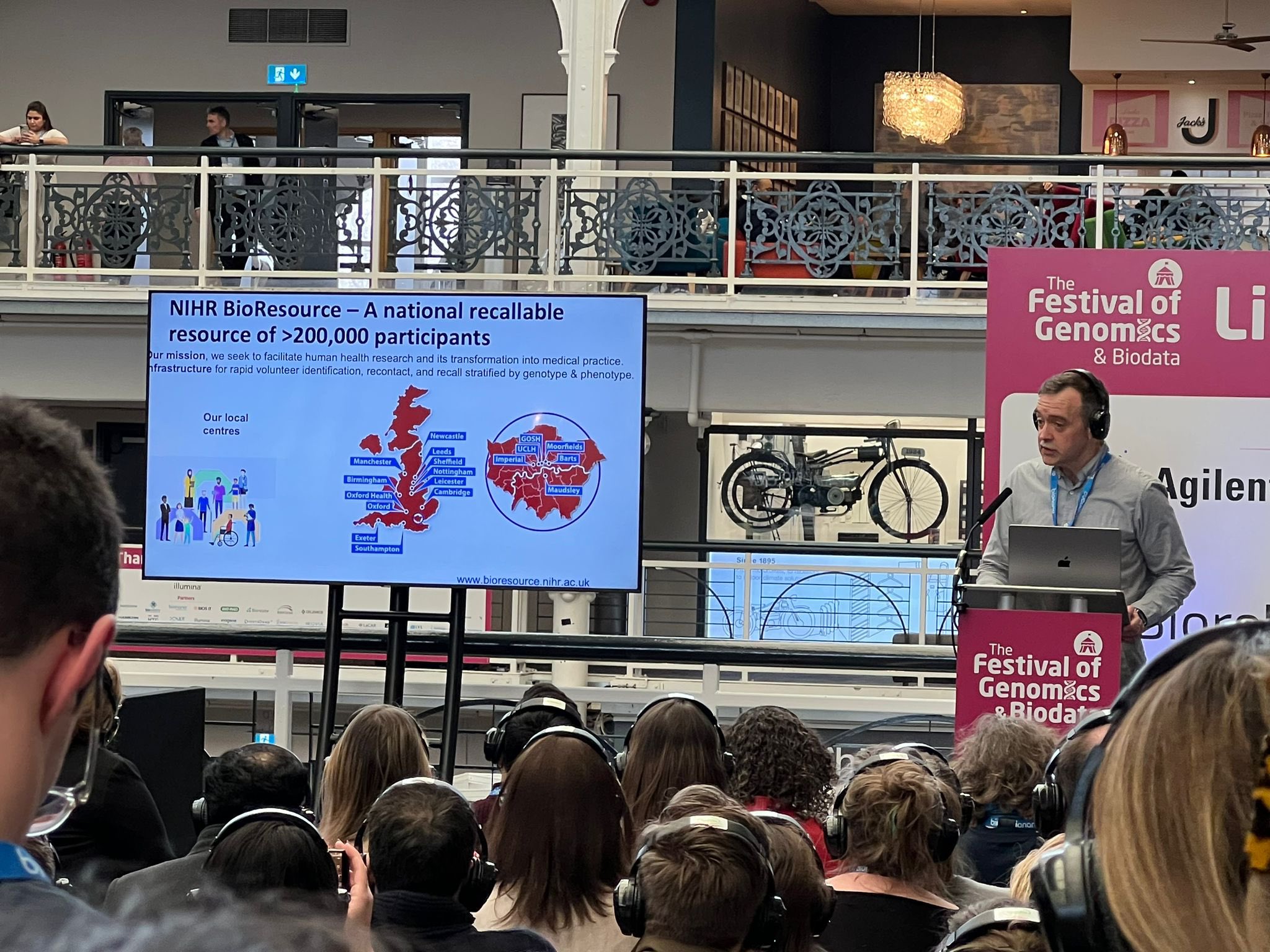 gerome-festival-of-genomics.jpg Professor Gerome Breen on stage at the festival in front of busy audience using headphone system to listen in