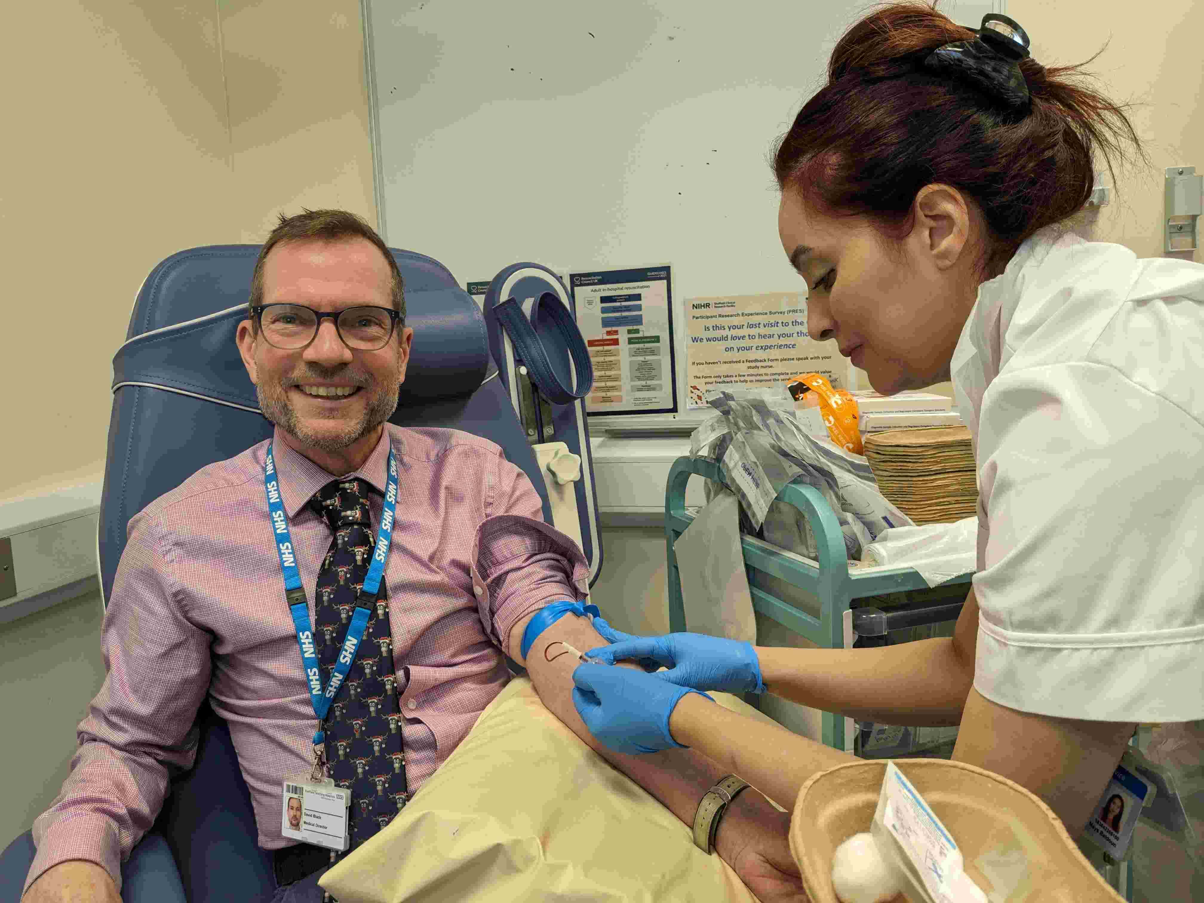 photo of: Dr David Black, Medical Director (Development) Sheffield Teaching Hospitals NHS Foundation Trust smiling while getting blood sample taken from nurse, volunteered to be recruited to the NIHR BioResource