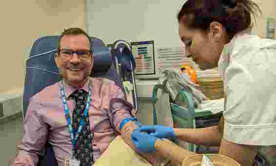 photo of: Dr David Black, Medical Director (Development) Sheffield Teaching Hospitals NHS Foundation Trust smiling while getting blood sample taken from nurse, volunteered to be recruited to the NIHR BioResource