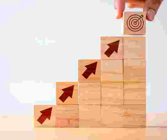 Stacked wooden blocks with arrows pointing upwards to indicate progress and target