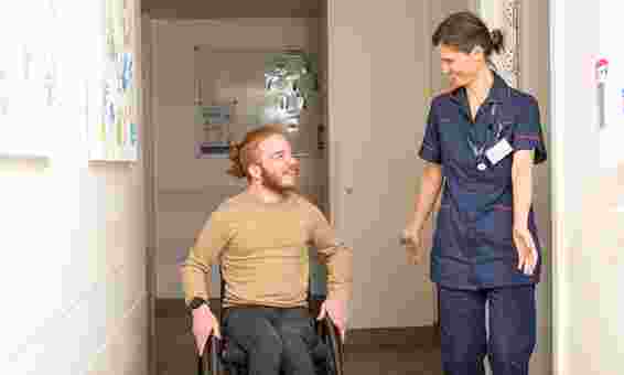 photo of: male disabled person in wheelchair greeted and speaking to clinican at S2 clinic both smiling