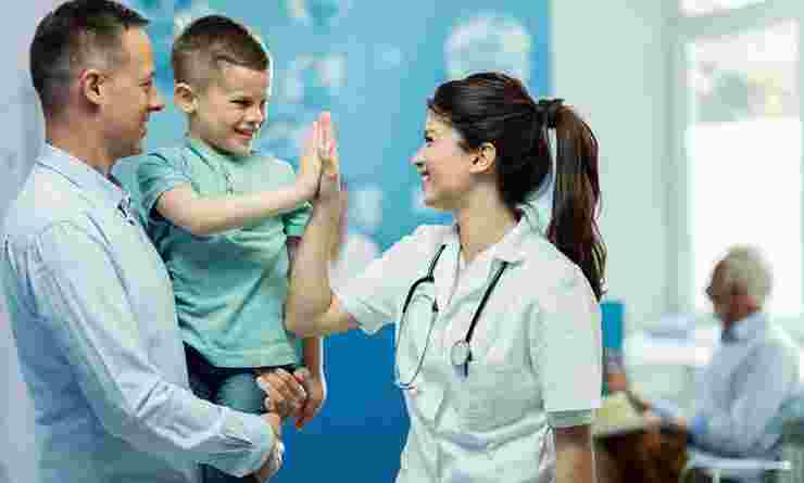 Medical staff member high fives boy in male adult's arms