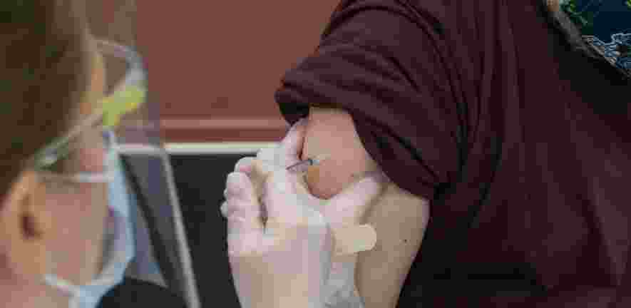Healthcare worker in gloves, facemask and face shield inserting needle into patient's arm